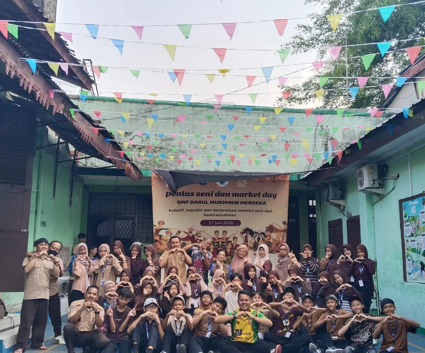 Pengurus OSIS dan para guru membentuk hati dengan tangan di bawah rangkaian bendera hias